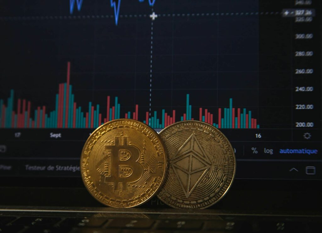 Deux pièces Bitcoin devant un écran d'analyse de cours de cryptomonnaies